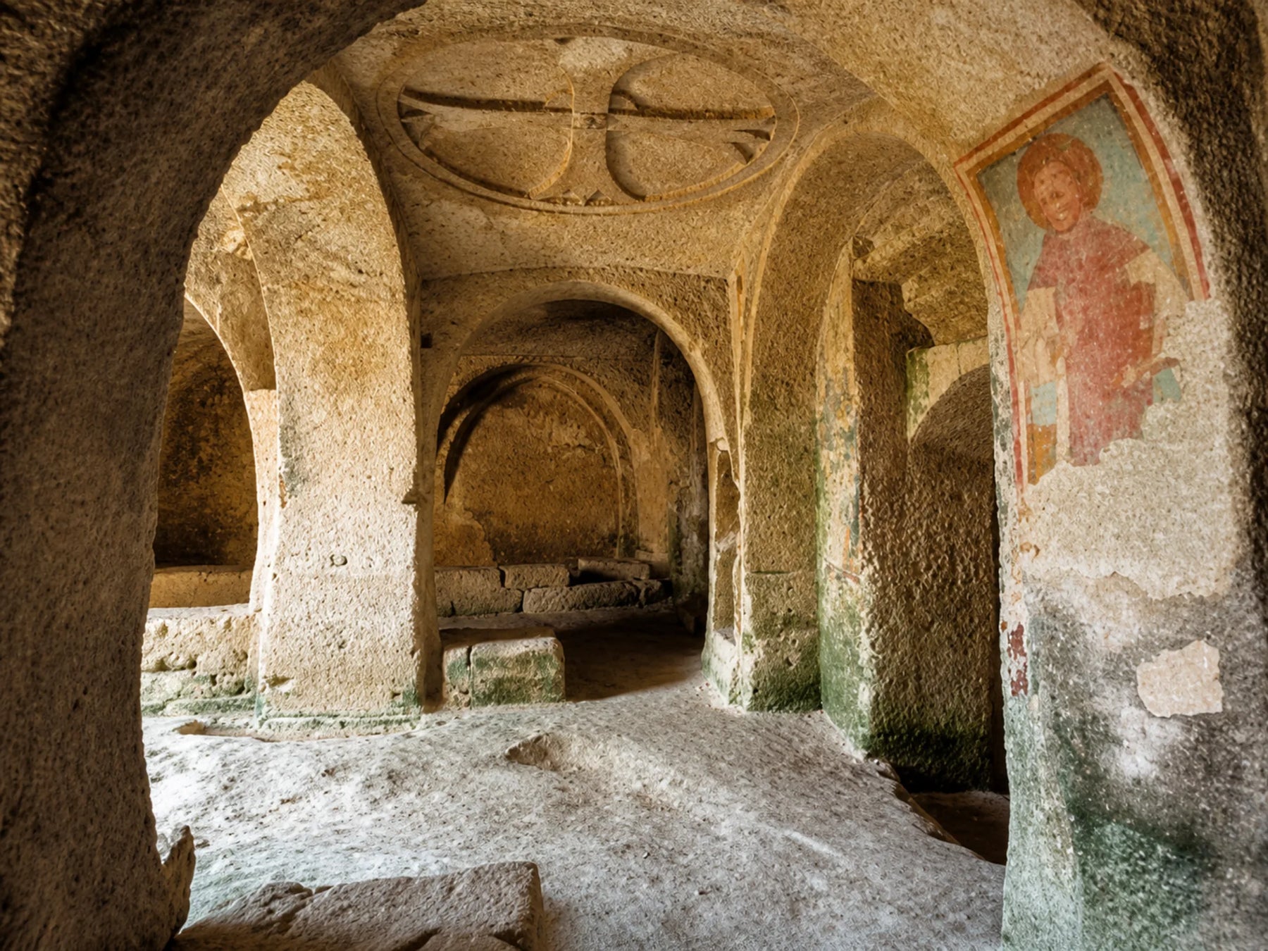 Interno di una chiesa rupestre a Matera con archi scavati nella roccia e affreschi sulle pareti