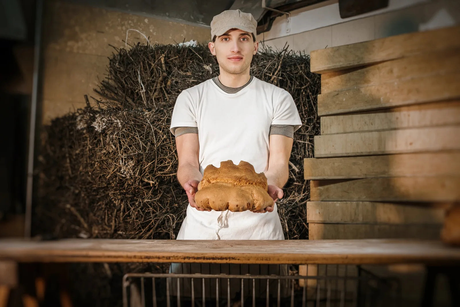 Fornaio in laboratorio che tiene tra le mani un pane artigianale appena preparato.