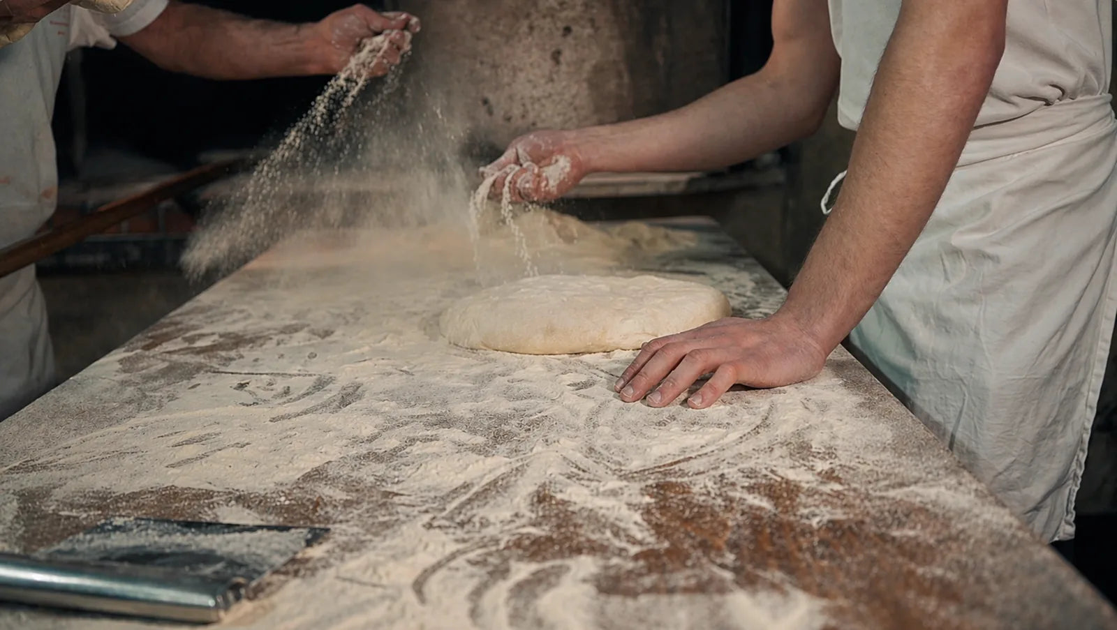 Farina sparsa sul banco da lavoro mentre i fornai preparano a mano l’impasto del pane.
