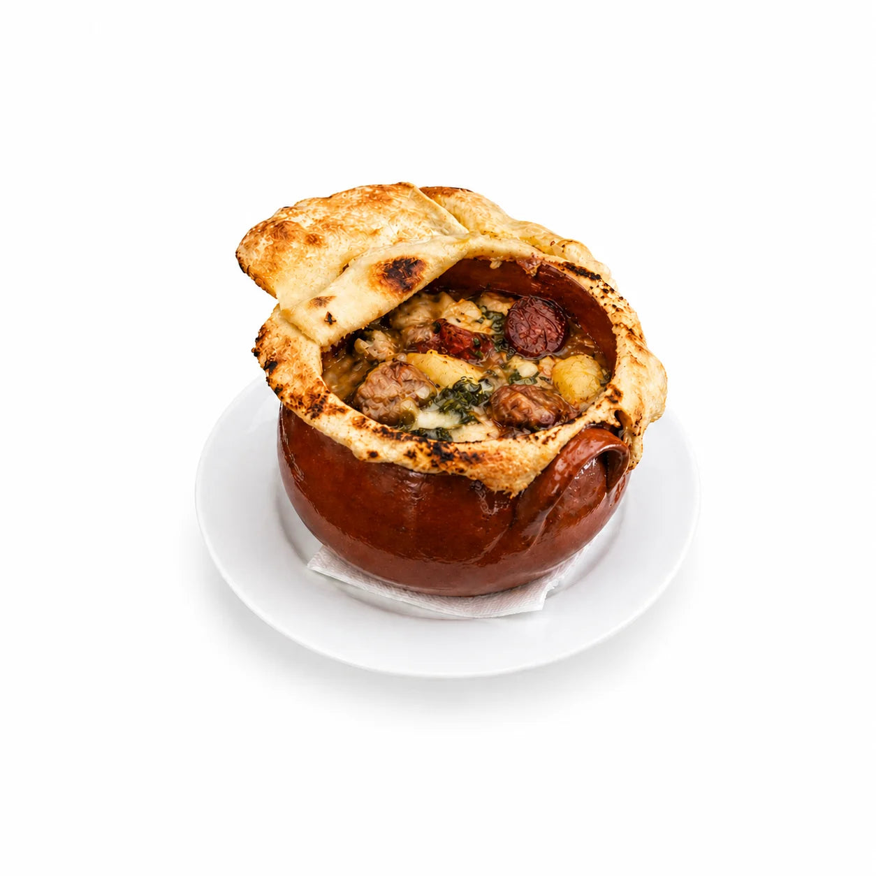 Pignata materana in vaso di terracotta con copertura di pasta di pane aperta, ripiena di carne di pecora, patate, pomodoro, erbe aromatiche e fetta di soppressata, su piatto bianco e sfondo bianco.