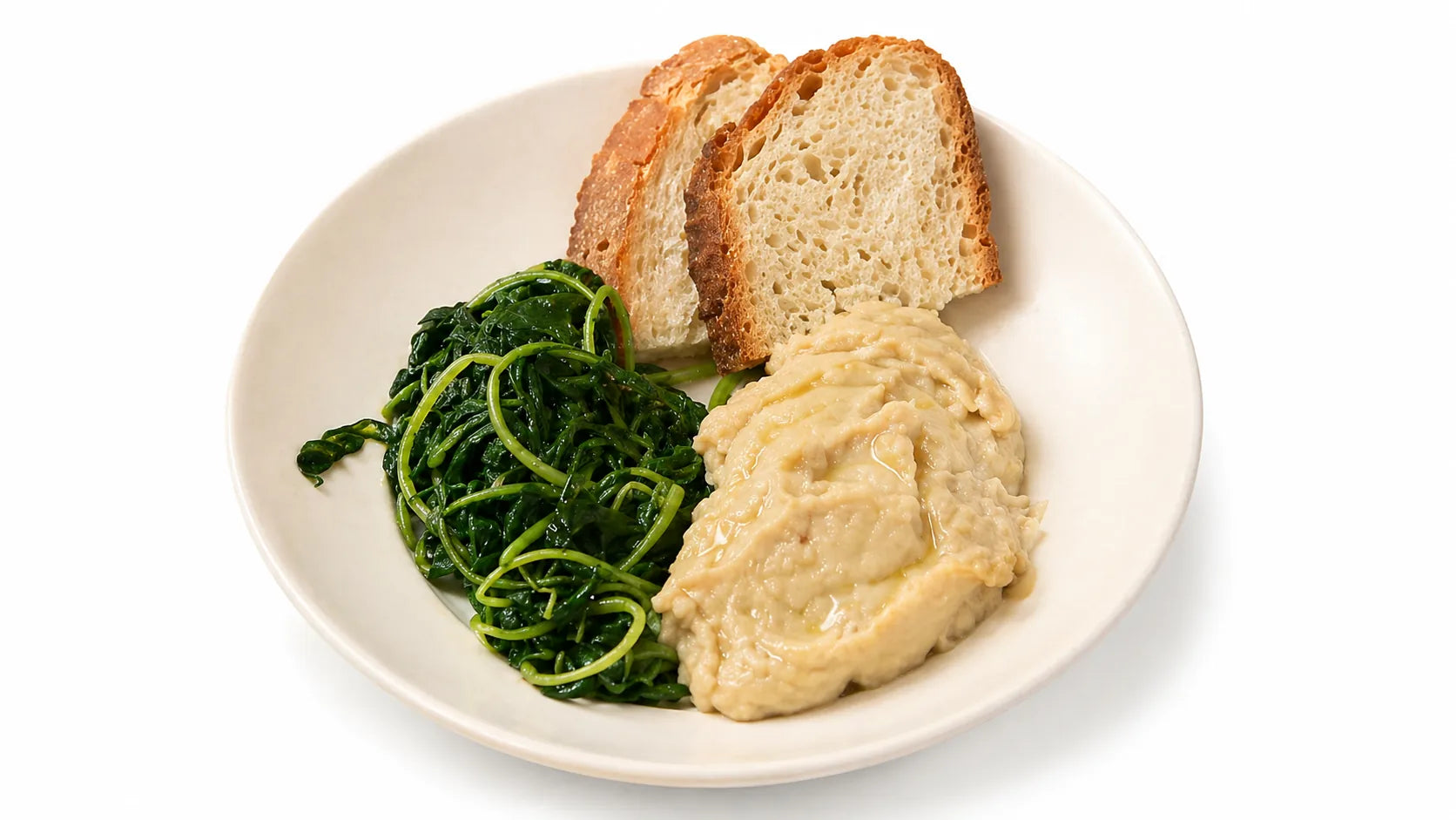 Purè di fave con cicoria selvatica saltata, un filo d’olio extravergine d’oliva e fette di pane in piatto color crema su sfondo bianco.