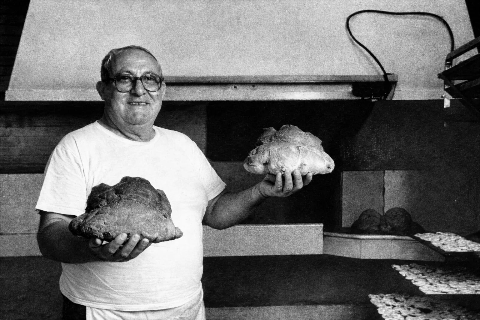 Santino Perrone mostra due pani artigianali davanti al forno in una foto storica in bianco e nero.